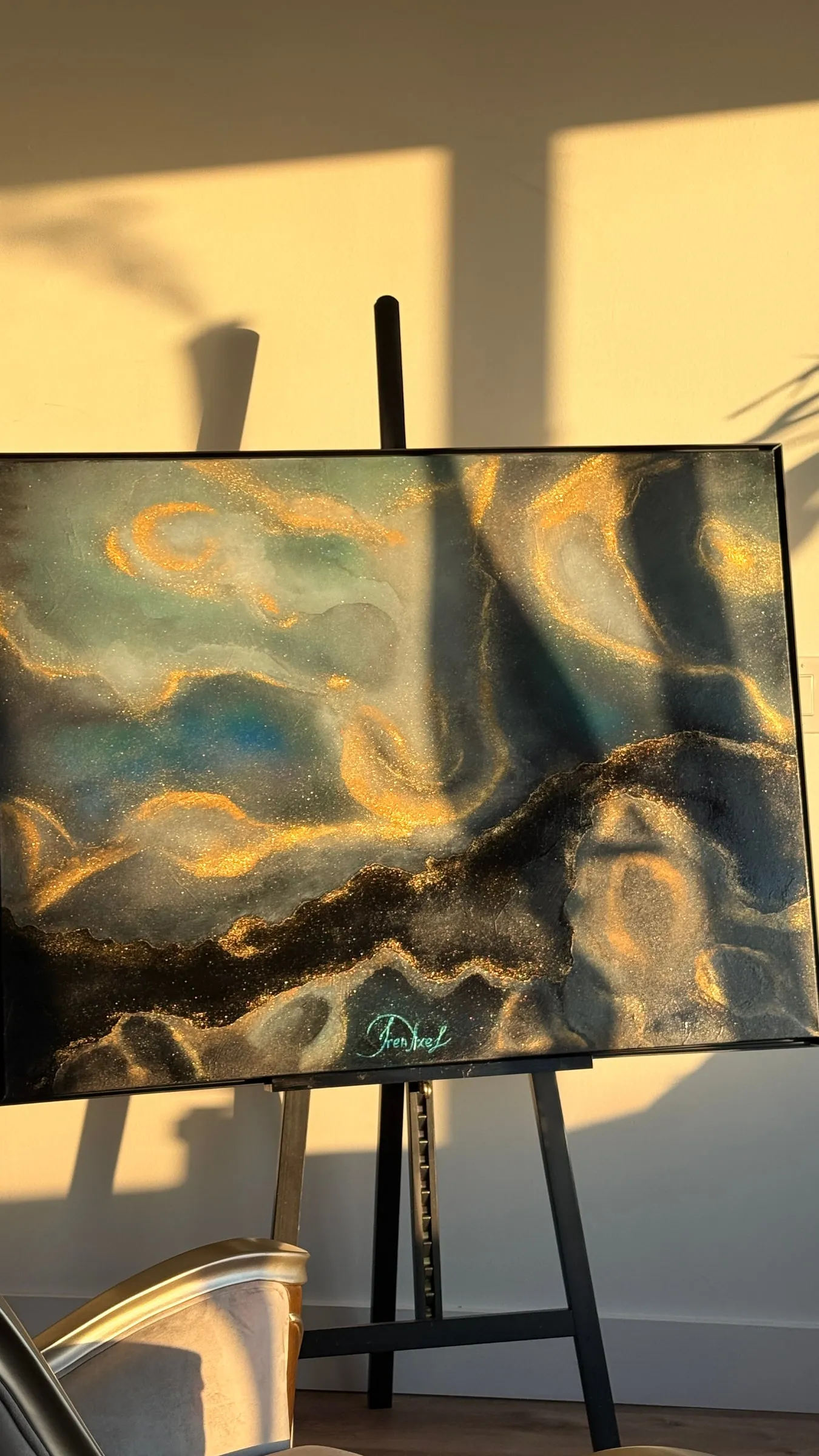 Dark abstract painting with gold and blue marbling, photographed on an easel